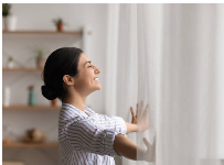 Mulher abrindo as cortinas para a luz da manhã